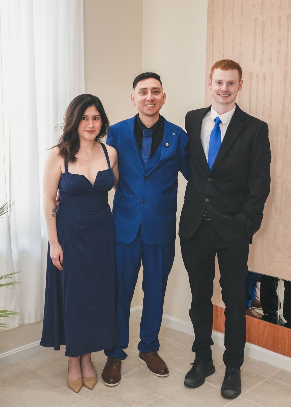 Three adults posing at a wedding, two men and a woman in coordinating navy blue formal attire.