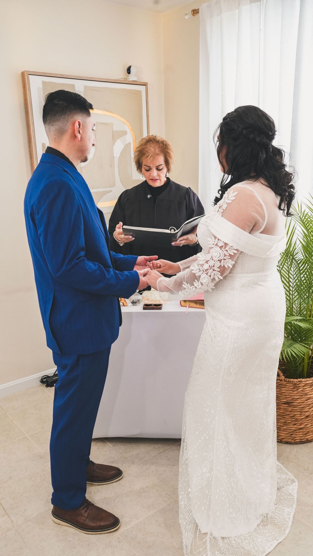 Couple exchanging vows at intimate wedding ceremony with officiant reading from book at white draped altar.