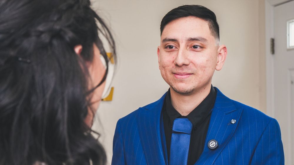 Man in blue suit and tie smiling warmly during a wedding ceremony.