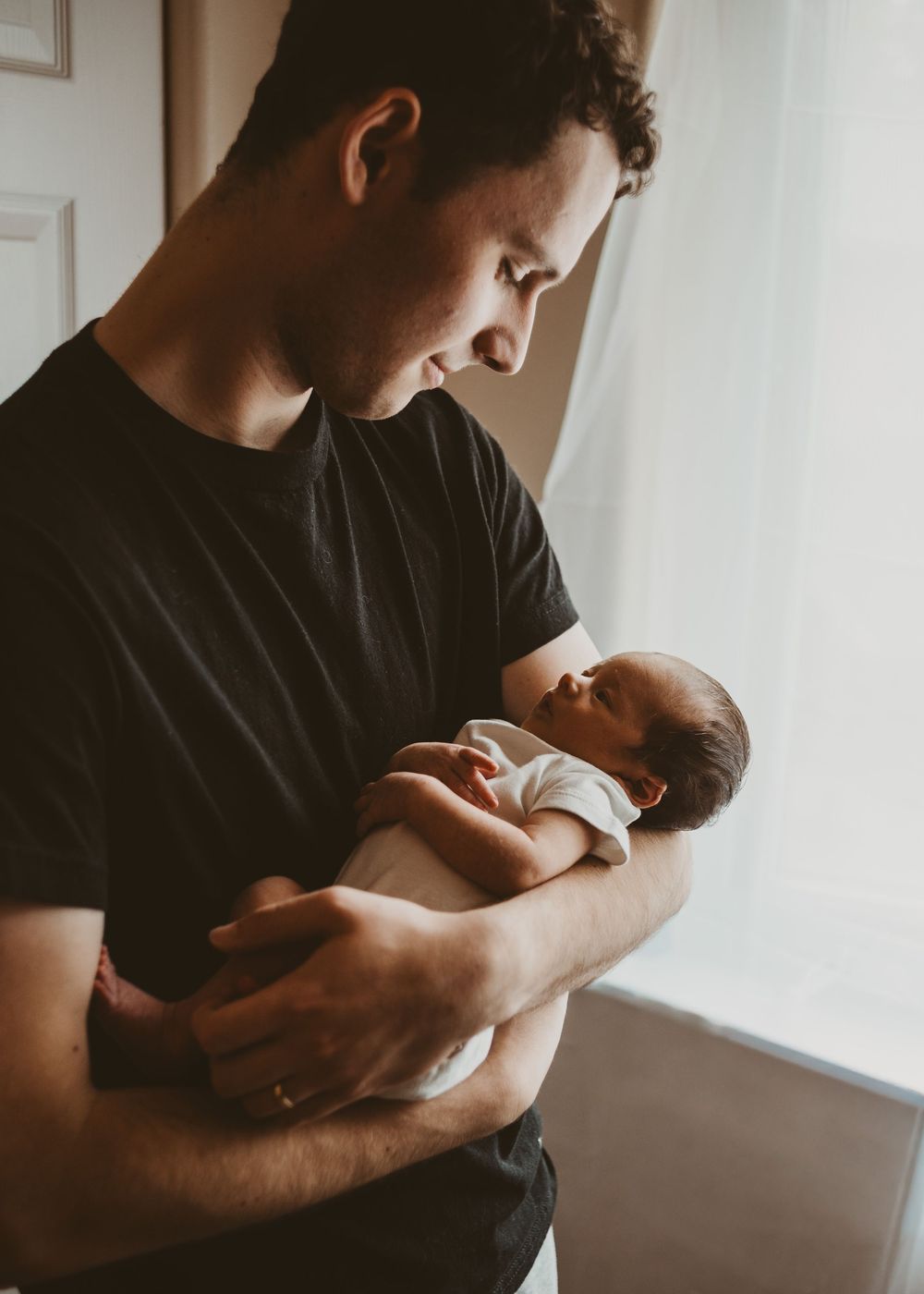 Father gently holding his newborn baby near a window during an in-home newborn session