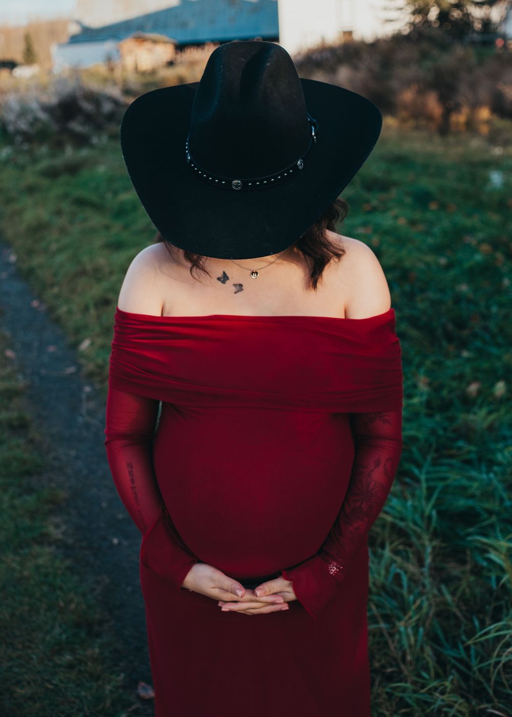 Pregnant woman wearing a red dress and black hat standing outdoors during a maternity session