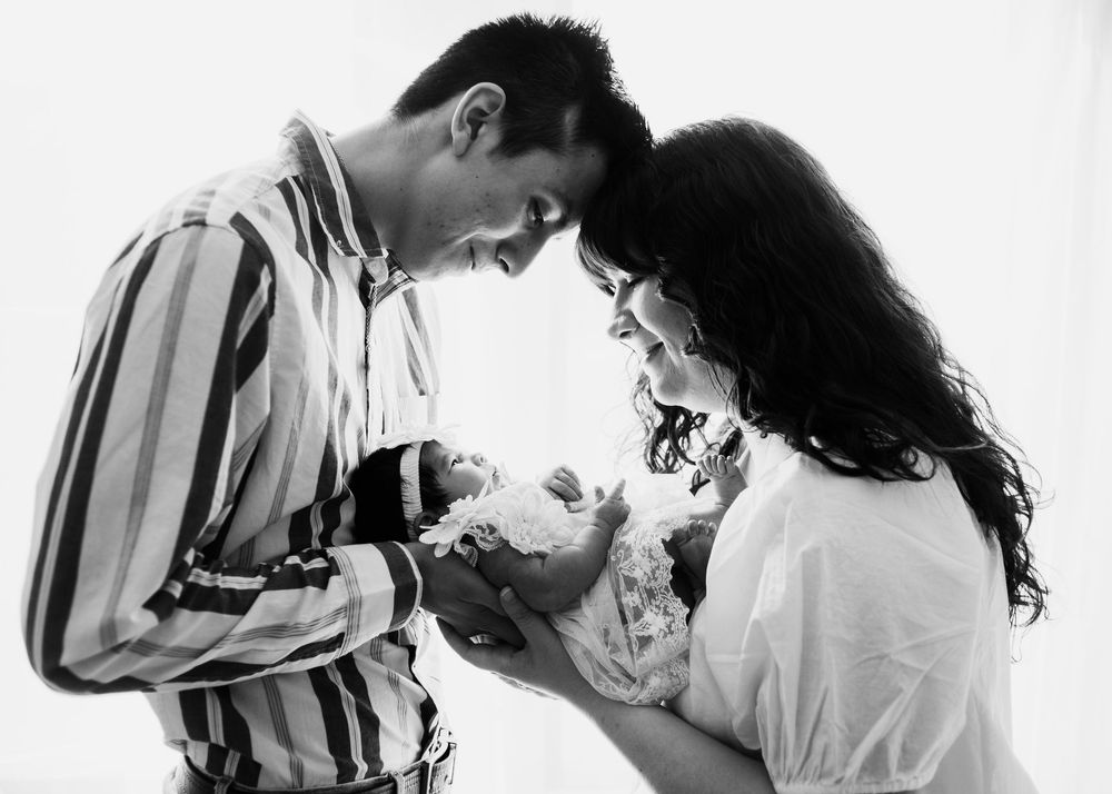 Black and white portrait of parents gently holding and looking at their newborn baby together