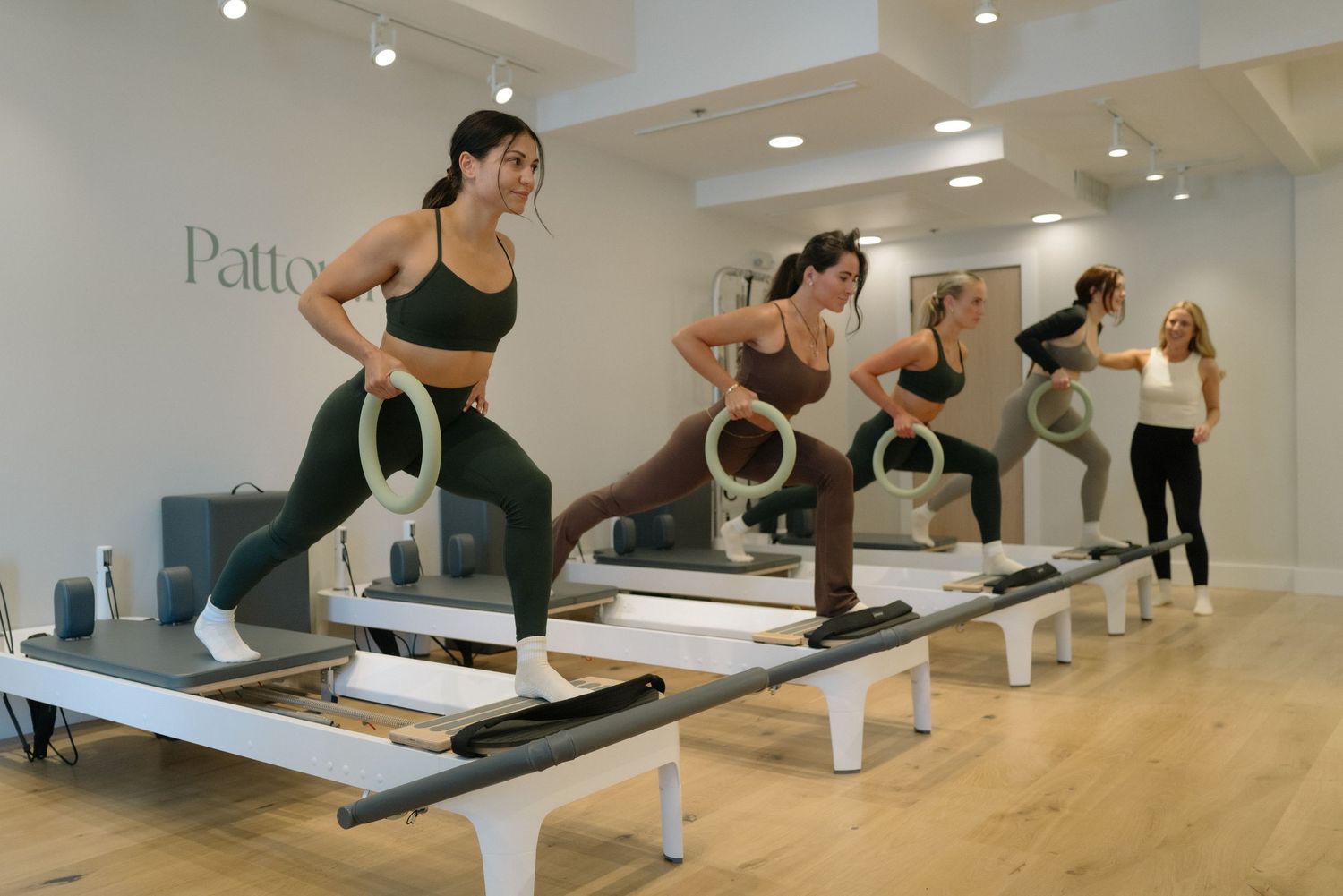 Women performing Pilates exercises on reformer machines in a bright modern studio with ring props.