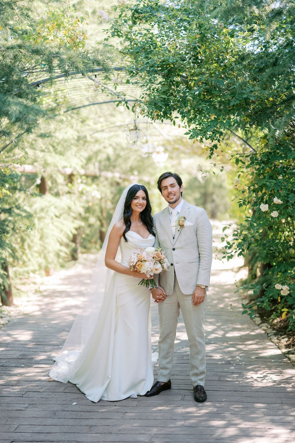 Bride and groom portrait on a wooden walkway surrounded by lush green trees on their wedding day.
