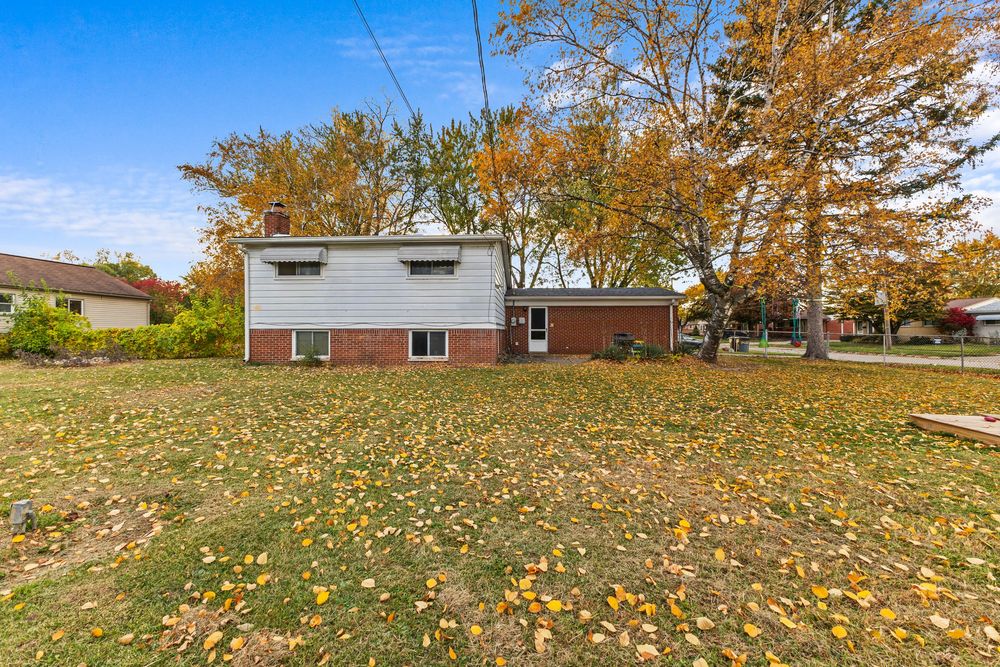 Front exterior of split-level brick and vinyl home with large lawn covered in fall leaves.
