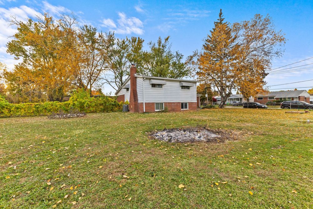 Side exterior of brick and vinyl home with chimney and expansive green lawn in autumn.