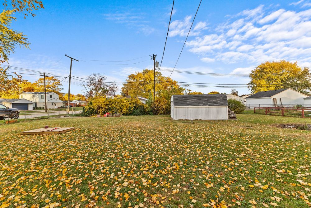 Large grassy yard with detached garage and colorful autumn trees under bright blue sky.