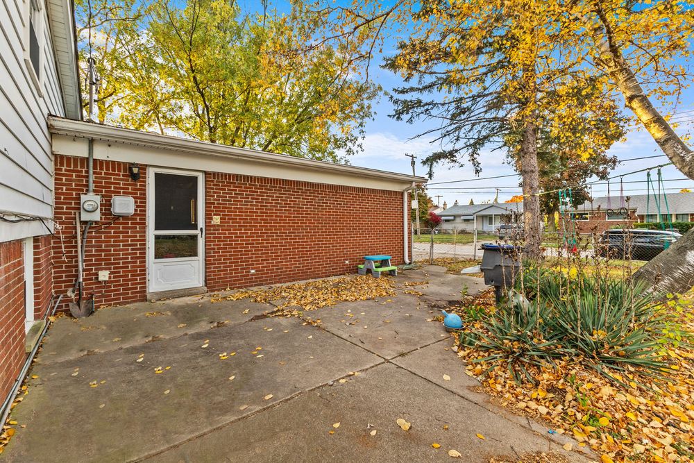 Brick exterior side of home with concrete patio, entry door, and fall foliage nearby.