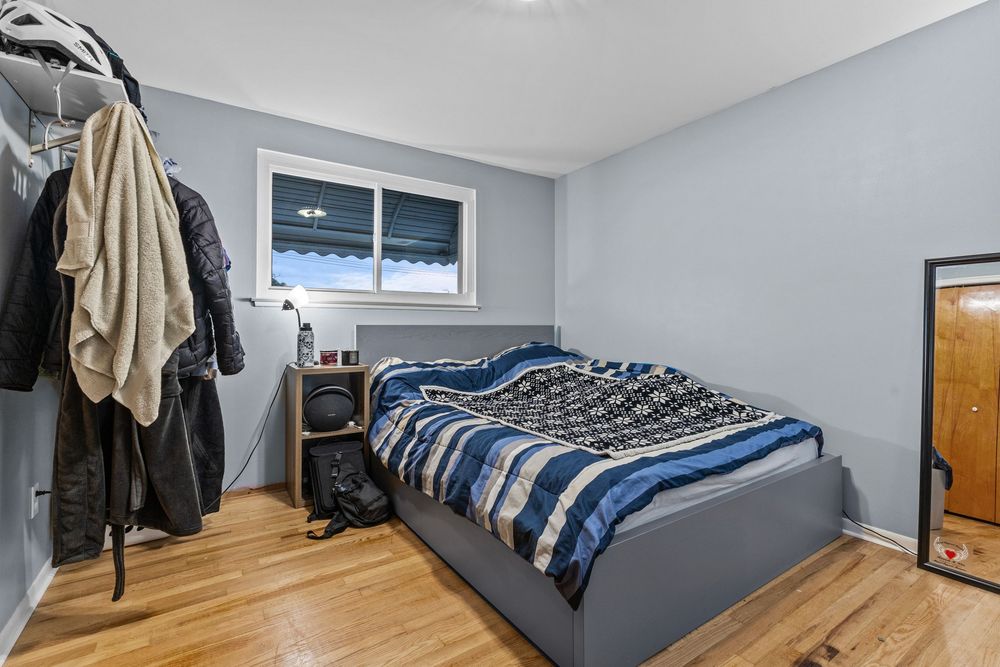 Bedroom with hardwood floors, gray platform bed, and open closet with natural window light.