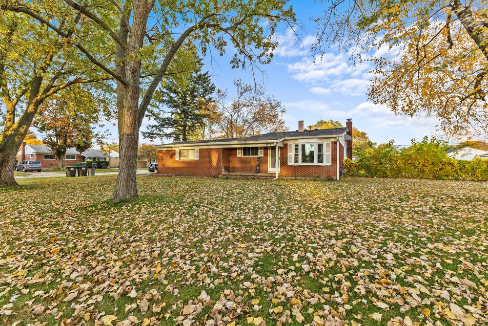 Single-story brick ranch house with wide front yard covered in fallen autumn leaves.