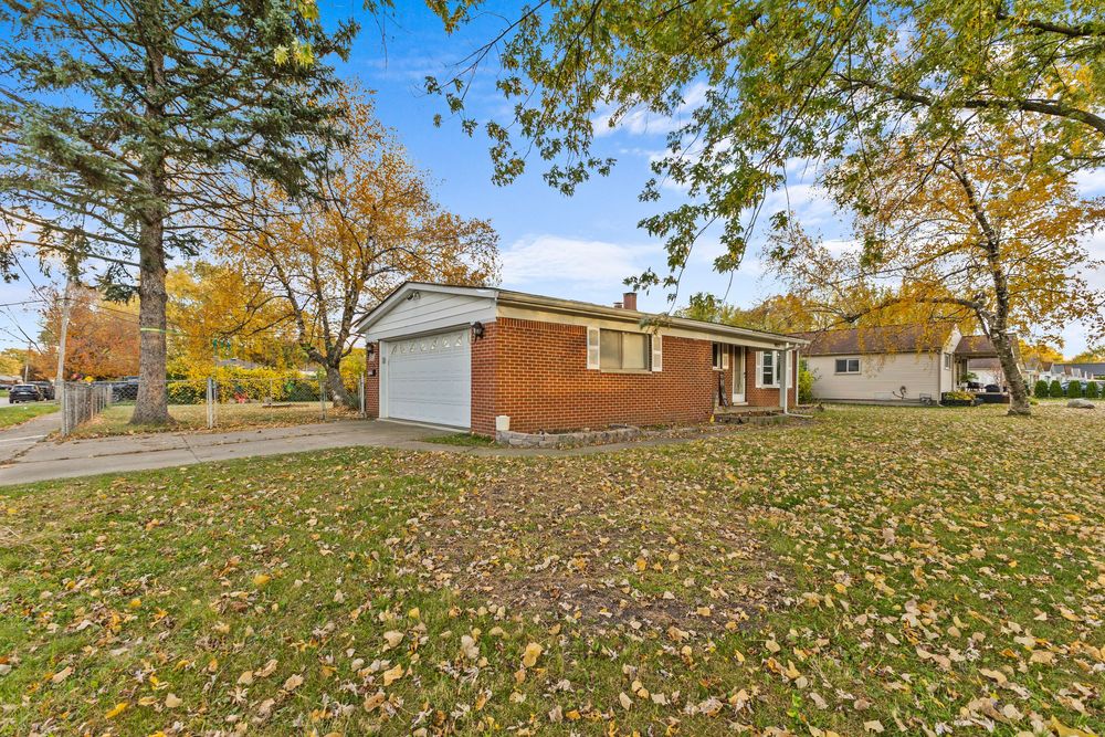 Brick ranch home with attached garage and large yard surrounded by fall foliage trees.
