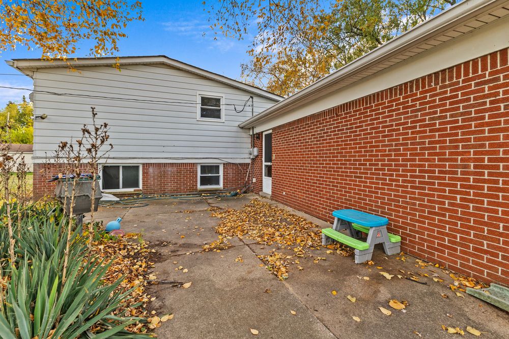 Side view of brick and vinyl home with patio area and autumn foliage in background.
