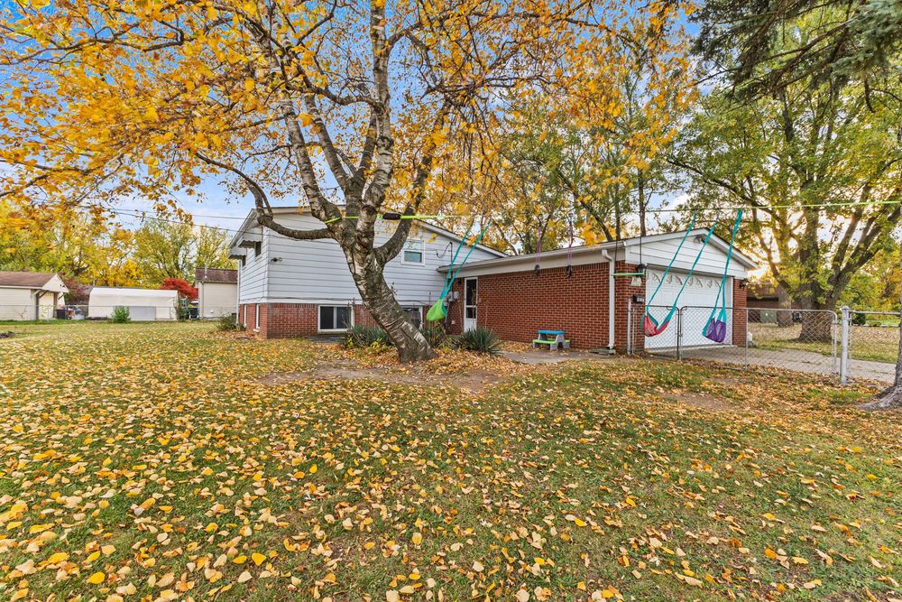 Rear view of brick home with large yard full of golden autumn leaves and mature trees.