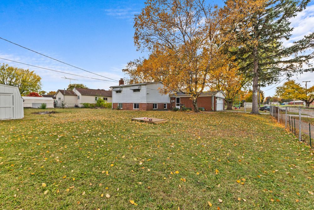 Spacious backyard of brick home with storage shed and wooden fence in autumn setting.