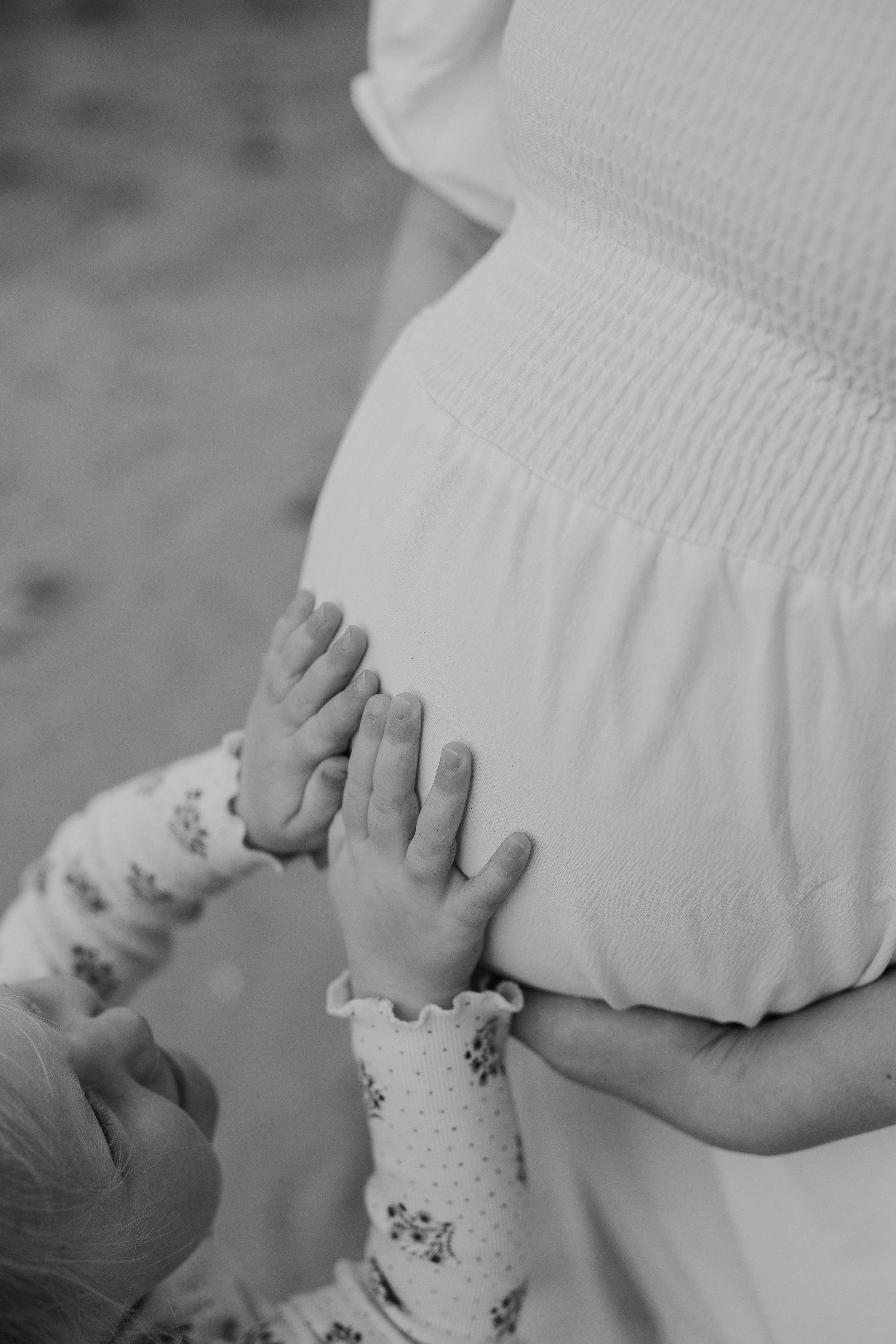 Family photo session on the beach. Maternity, family portrait at rabbit island. Black and white daughters hands on bump cropped.