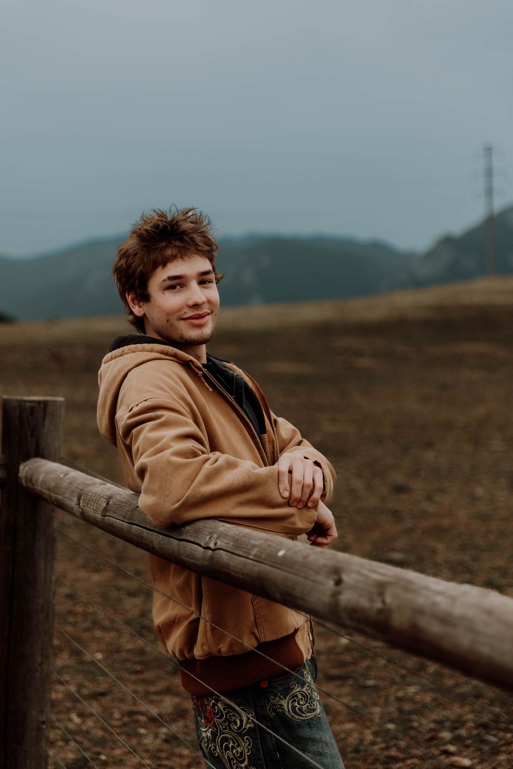 Boy leans on fence, and poses for senior photos, cinematic, mountain, and portrait photos in Boulder, Colorado outside and in nature