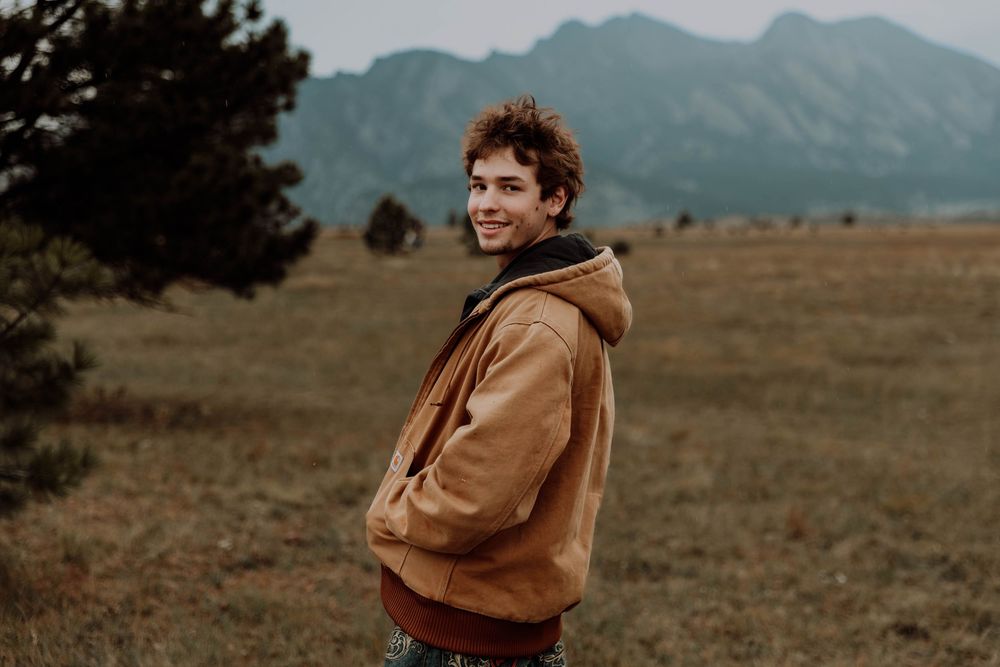 Boy turns back, smiles, and poses for senior photos, cinematic, mountain, and portrait photos in Boulder, Colorado outside and in nature