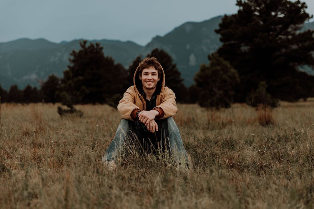 Boy sits down, smiles, and poses for senior photos, cinematic, mountain, and portrait photos in Boulder, Colorado outside and in nature
