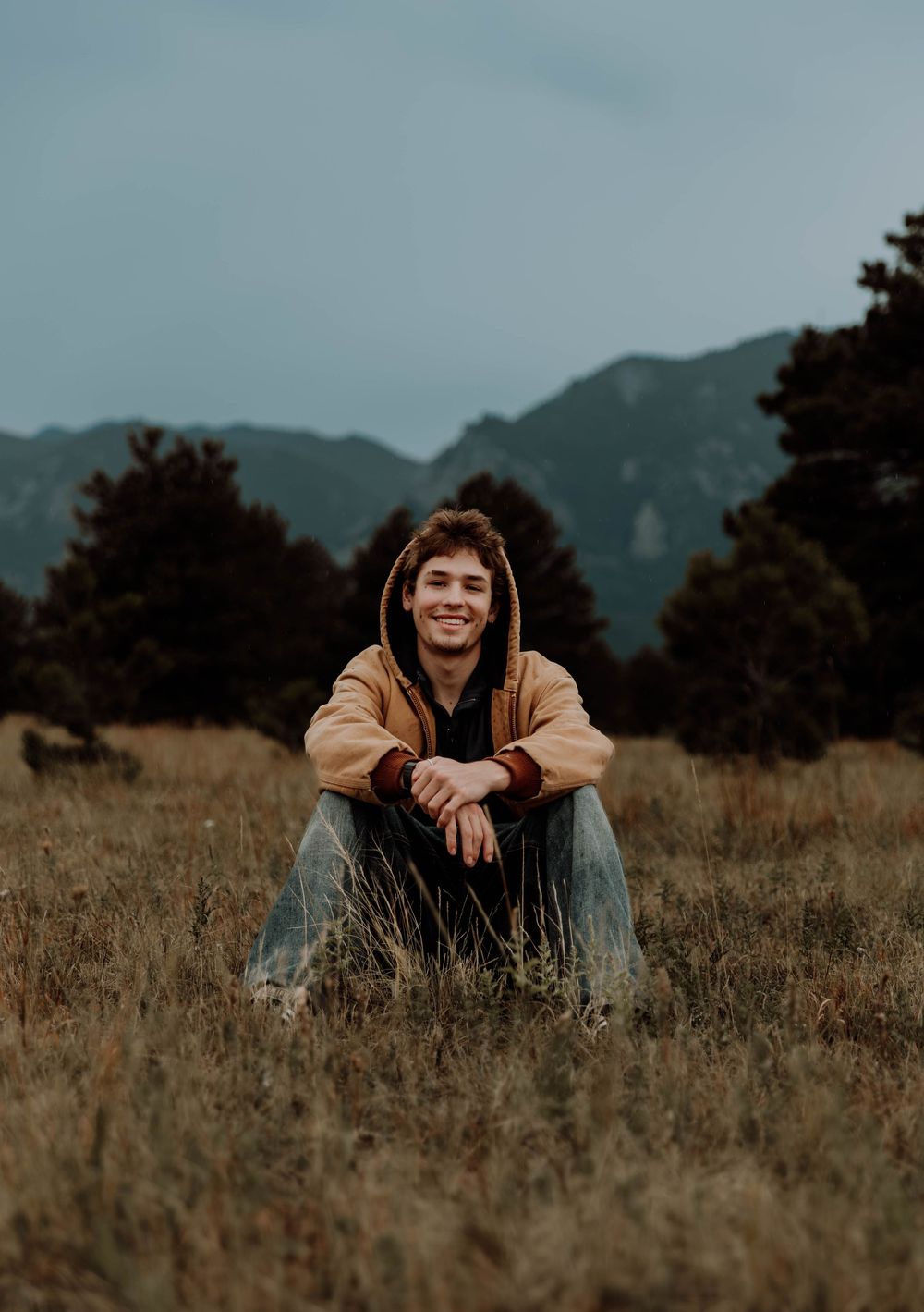 Boy sits down, smiles, and poses for senior photos, cinematic, mountain, and portrait photos in Boulder, Colorado outside and in nature