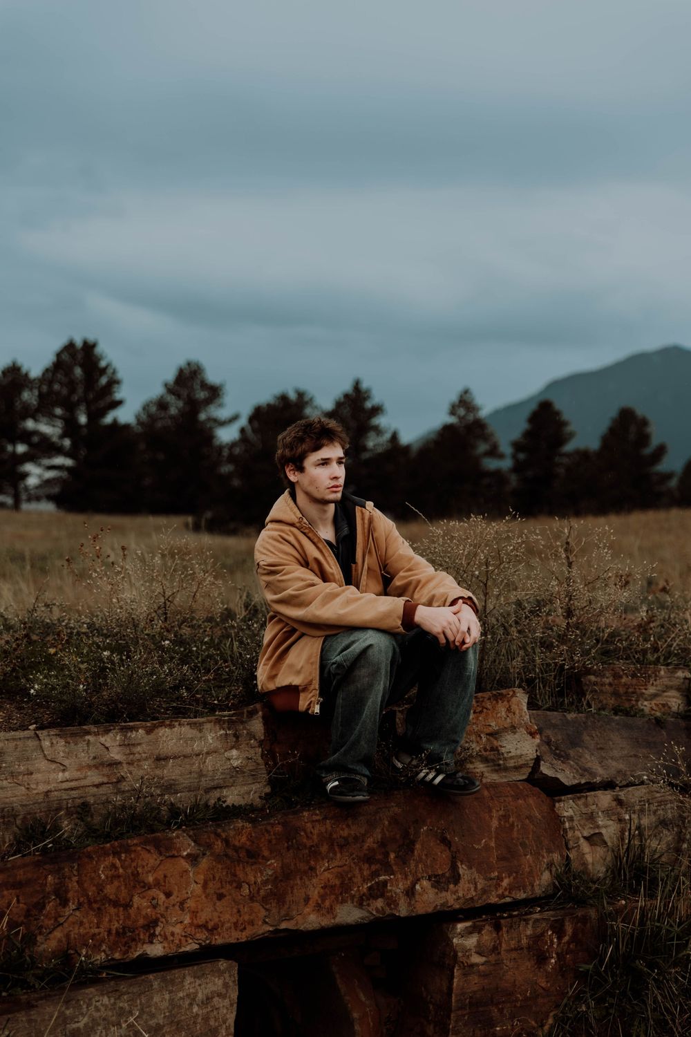Boy sits down, and poses for senior photos, cinematic, mountain, and portrait photos in Boulder, Colorado outside and in nature