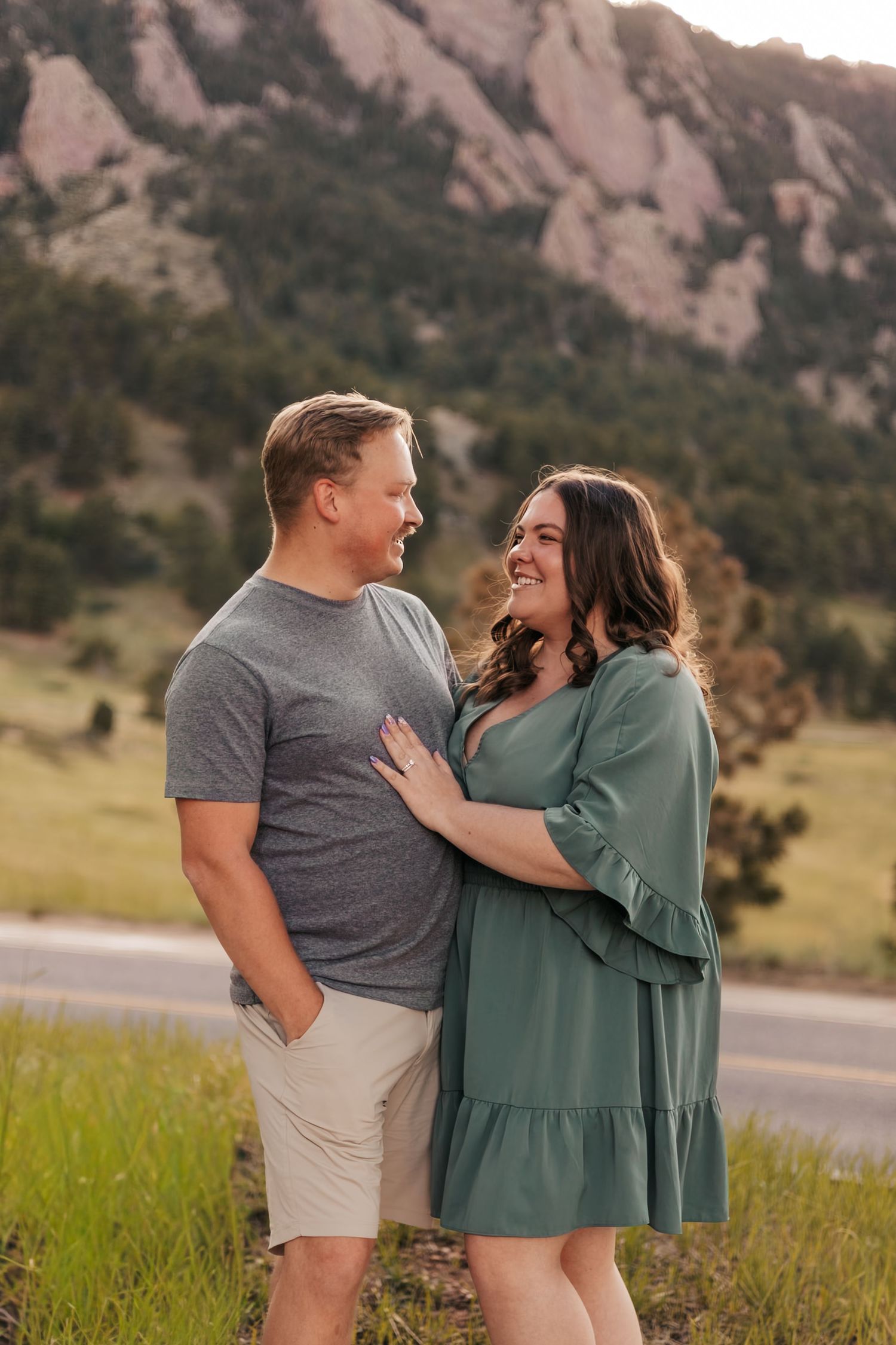 A smiling couple embraces outdoors with rocky mountain landscape  | Baby Announcement Photographer in Boulder, Colorado