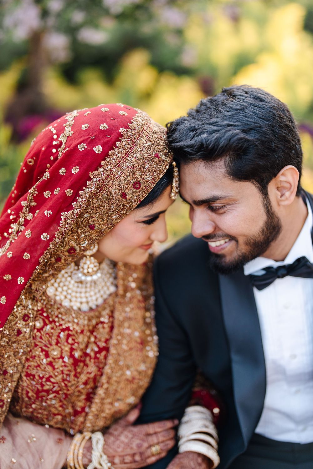 South Asian bride and groom in traditional wedding attire share an intimate moment, touching foreheads and smiling.