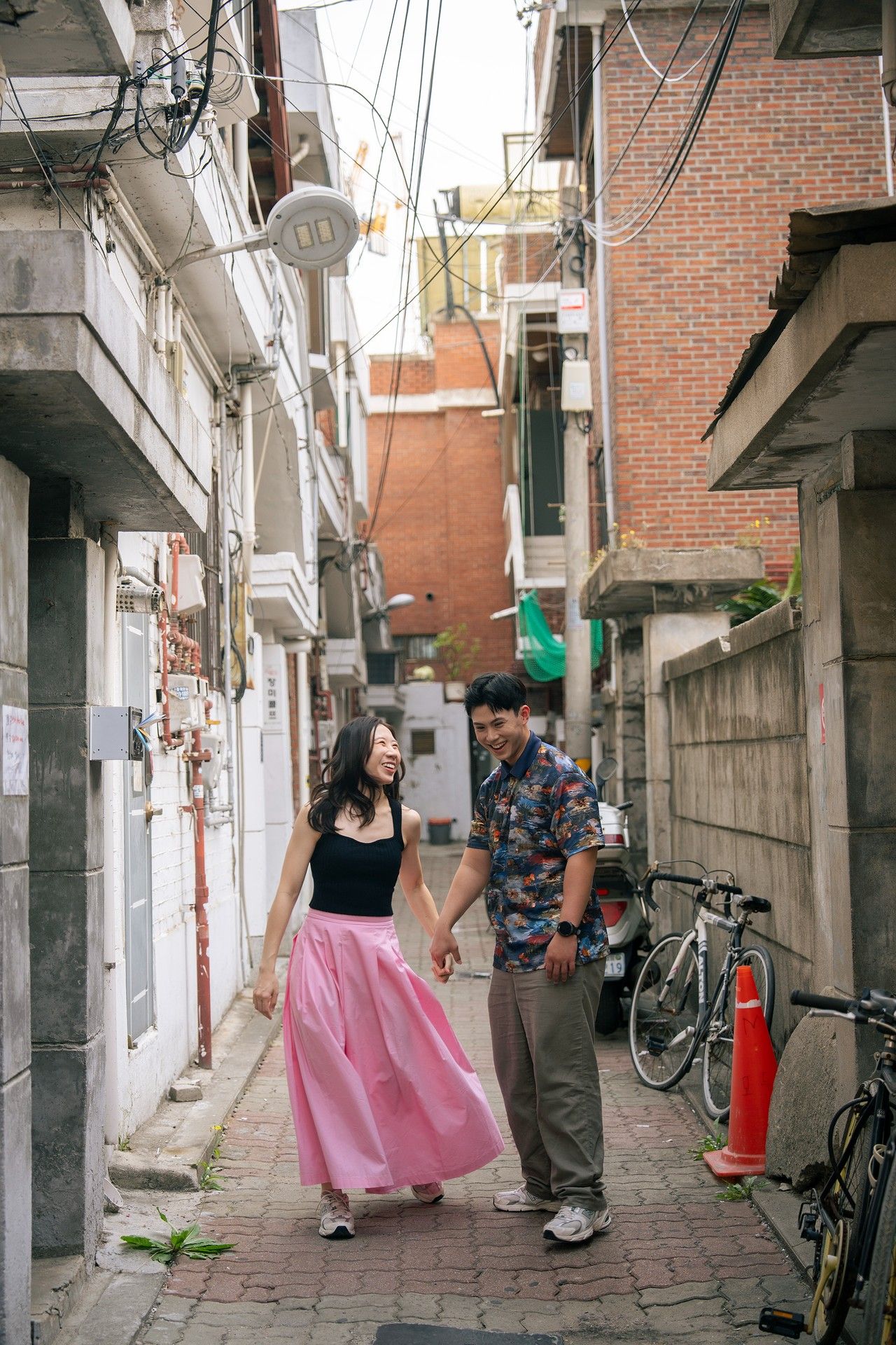 Couple holding hands while walking through a narrow urban alley, woman in pink skirt.