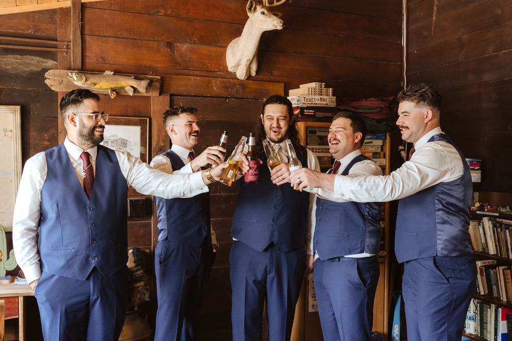 A groom and groomsmen in blue vests and pants cheers inside their getting ready cabin