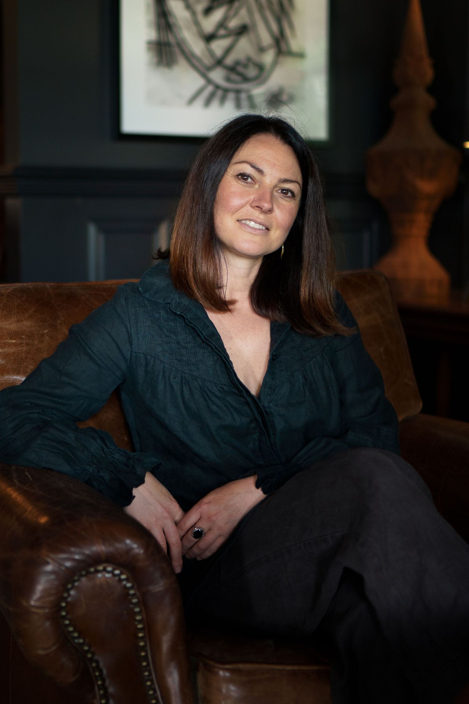 A brunette woman in a dark green blouse sits relaxed in a leather armchair in an elegant room.

Lou Chalmer