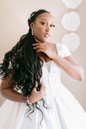 Beautiful bride with long braided hair in a white satin ballgown posing elegantly before her wedding ceremony.