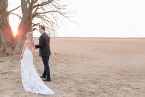 Bride and groom share romantic moment at golden sunset beside bare tree in open field.