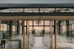 Elegant open-air wedding venue with glass walls, white chairs, and a stunning ocean sunset backdrop.