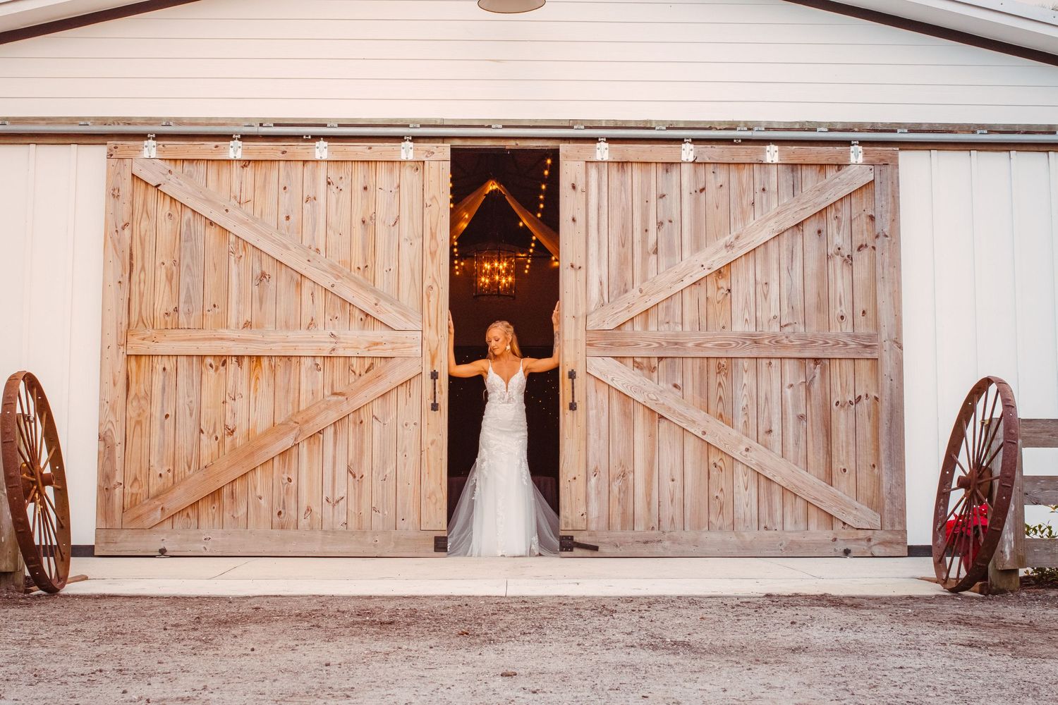 Bride stands between large barn doors posed for a rustic wedding portrait at The Barn at Palmetto Flats in Fort Pierce, FL