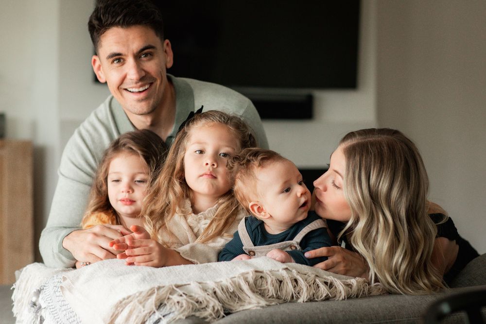 Father and four young children cuddling together on a couch, smiling at the camera.