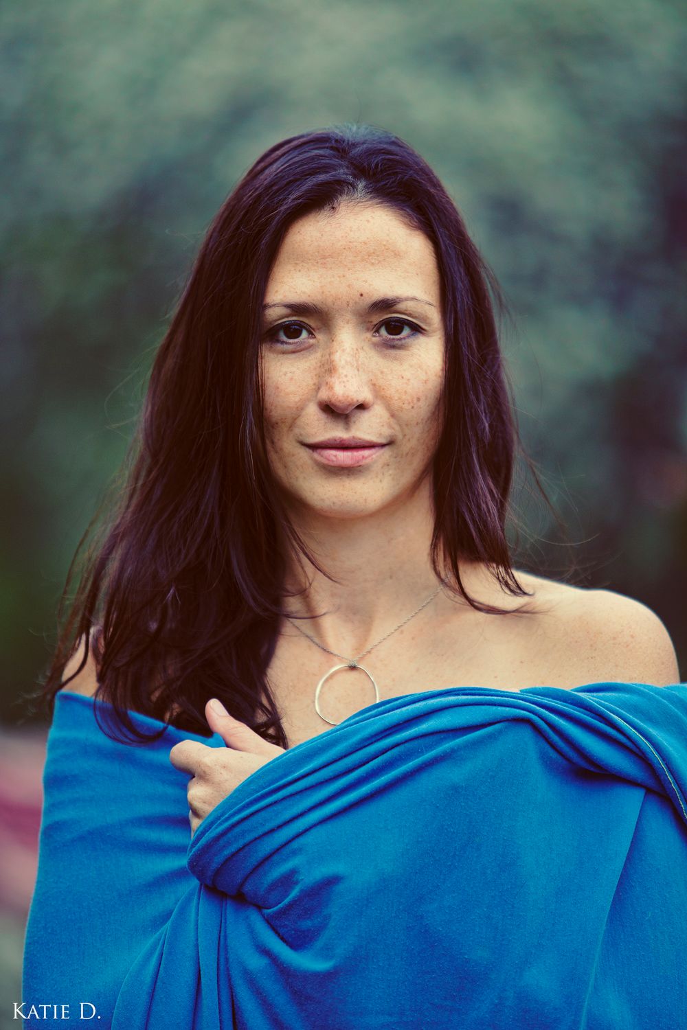 Close portrait of dark-haired woman with freckles in blue off-shoulder wrap outdoors.