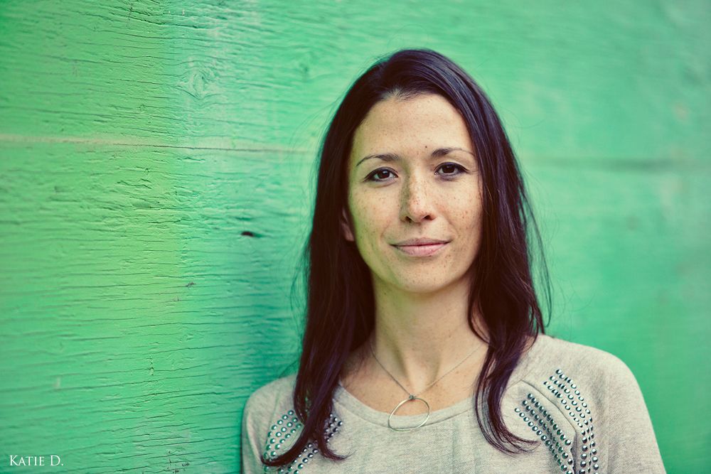 Portrait of dark-haired woman leaning against bright green painted wooden wall outdoors.