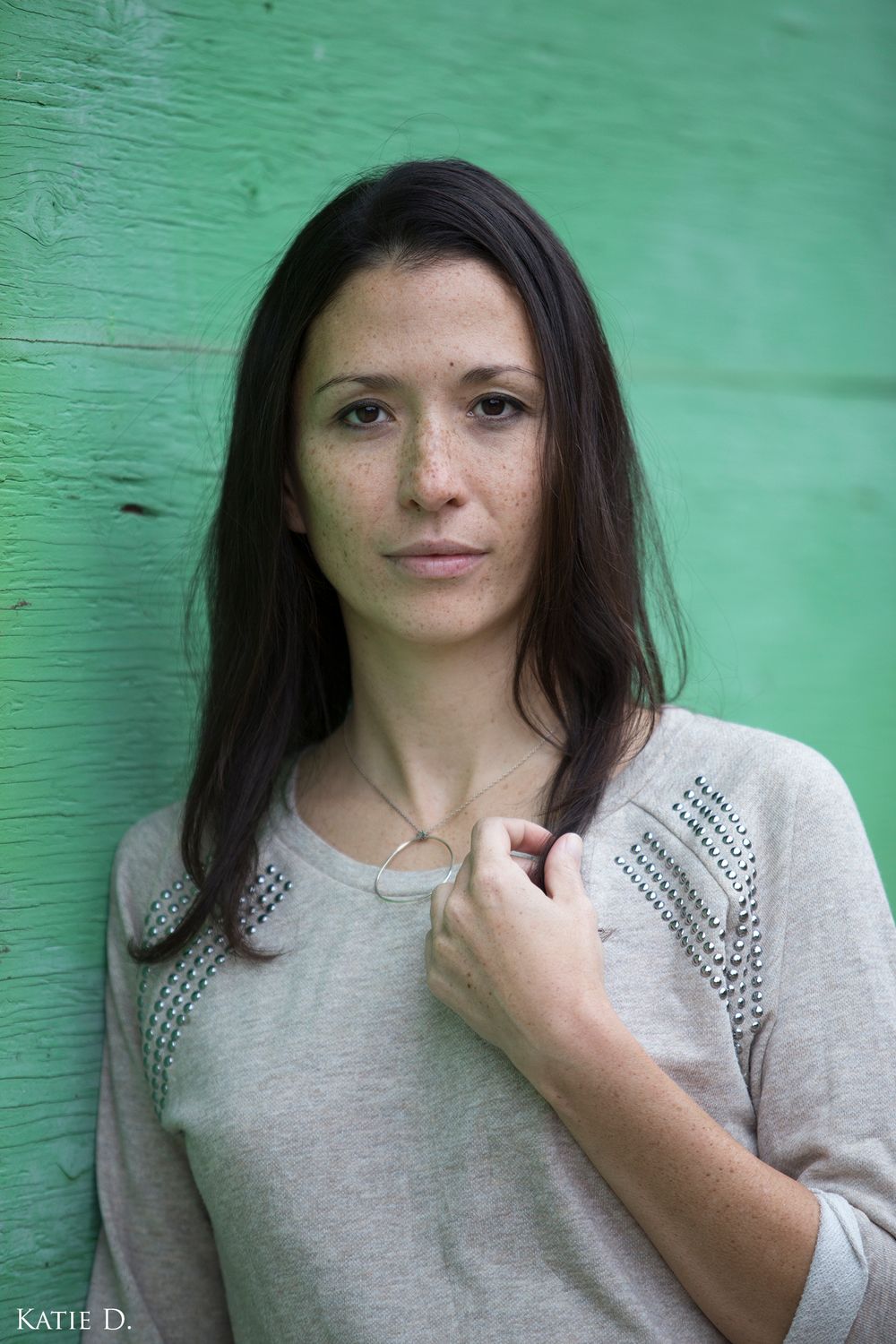 Close-up portrait of brunette woman in gray sweater against green wall.