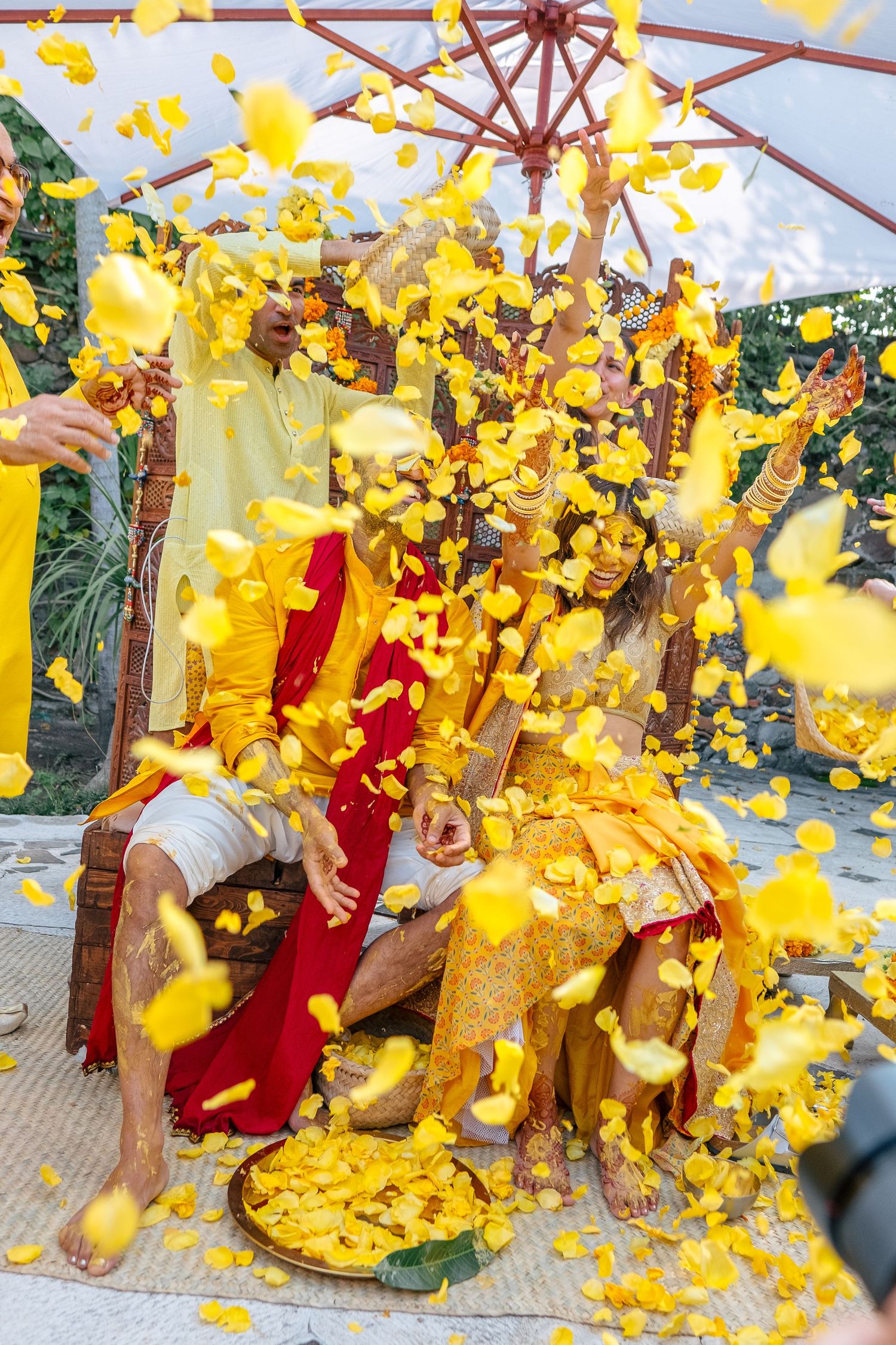 Indian couple in yellow outfits celebrating Haldi ceremony under stone arches with marigold petals.