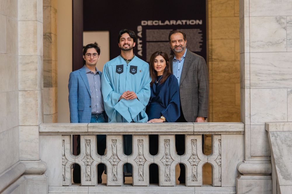 Four people posing together on a marble balcony near a Declaration exhibit in a formal building.