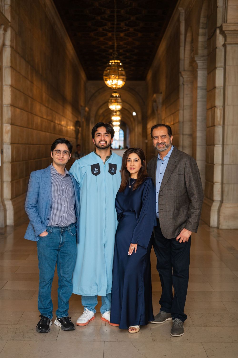 Family of four poses in elegant hallway during graduation celebration, graduate wearing light blue robe.