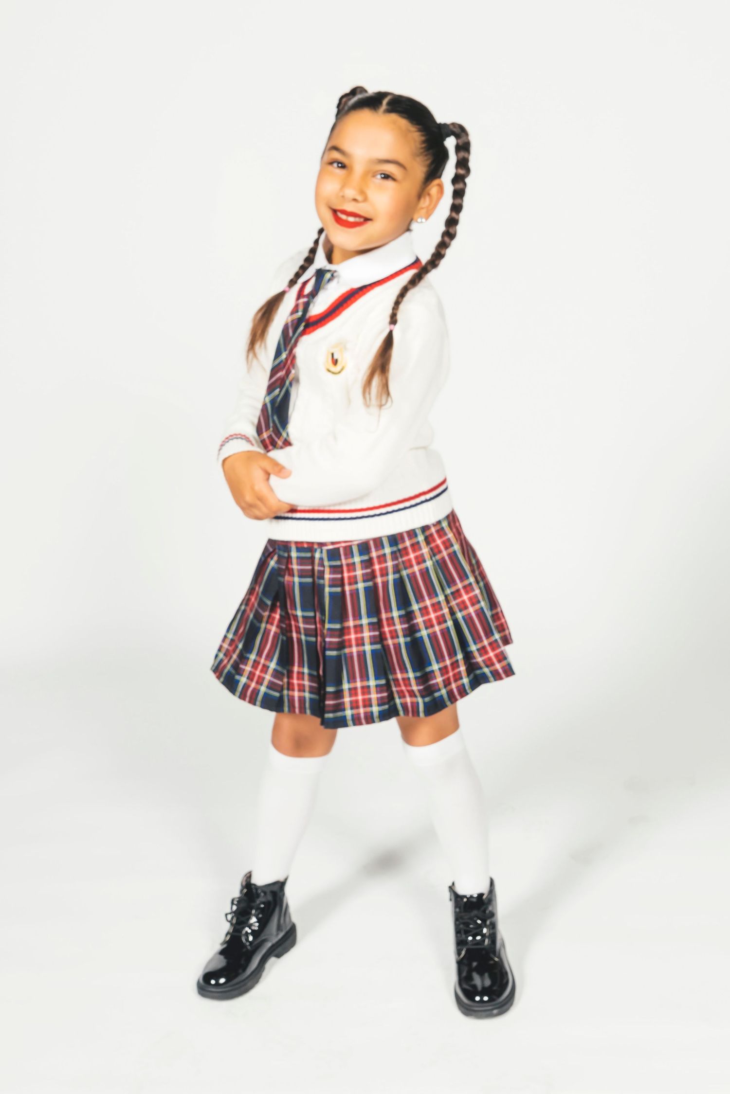 Young girl in school uniform with plaid skirt, white turtleneck, tie, knee socks, and black boots, posing confidently.