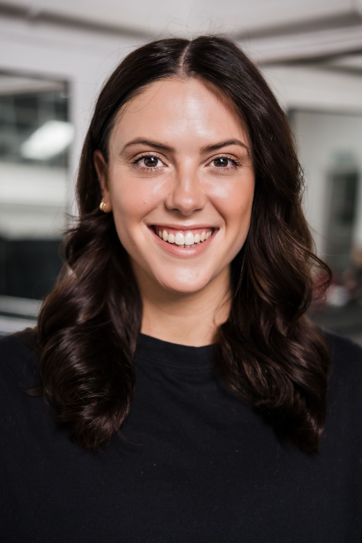 Smiling young woman with dark wavy hair wearing a black top in a professional headshot photo.