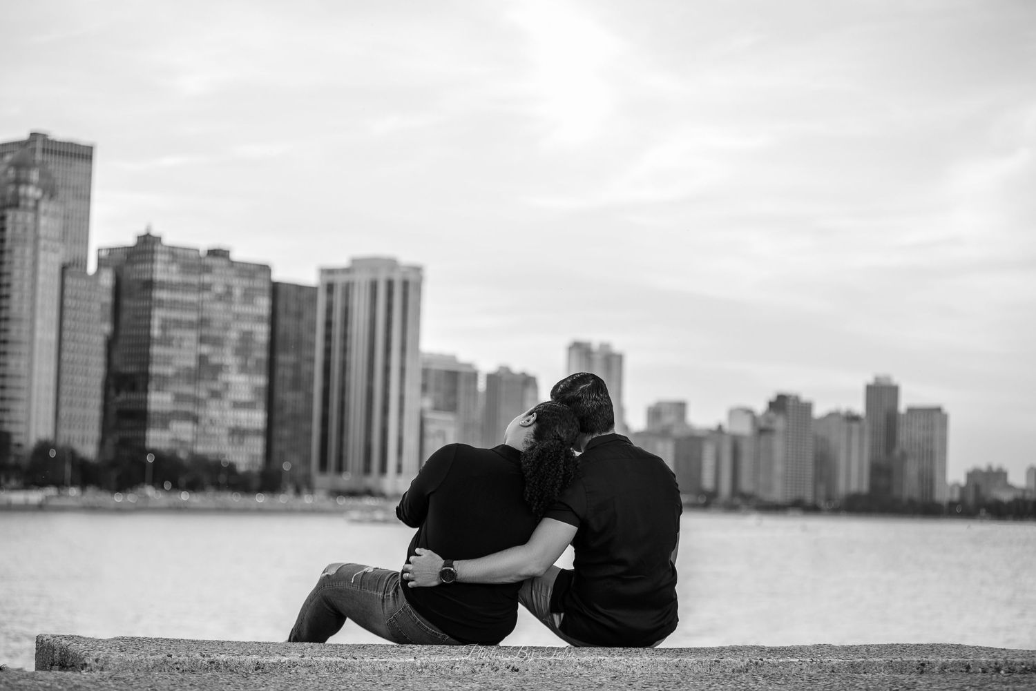 Woman in black coat and leather pants poses by Chicago waterfront with iconic Willis Tower skyline backdrop.