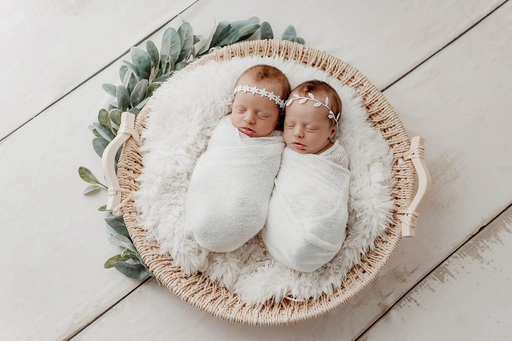 Two newborn twins swaddled in white wraps with floral headbands by Murrieta newborn twins photographer.