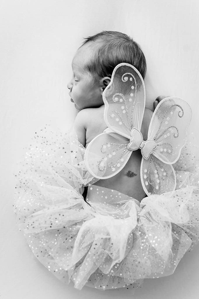 Newborn baby sleeping in fairy costume with butterfly wings and sparkly tutu, black and white photo.