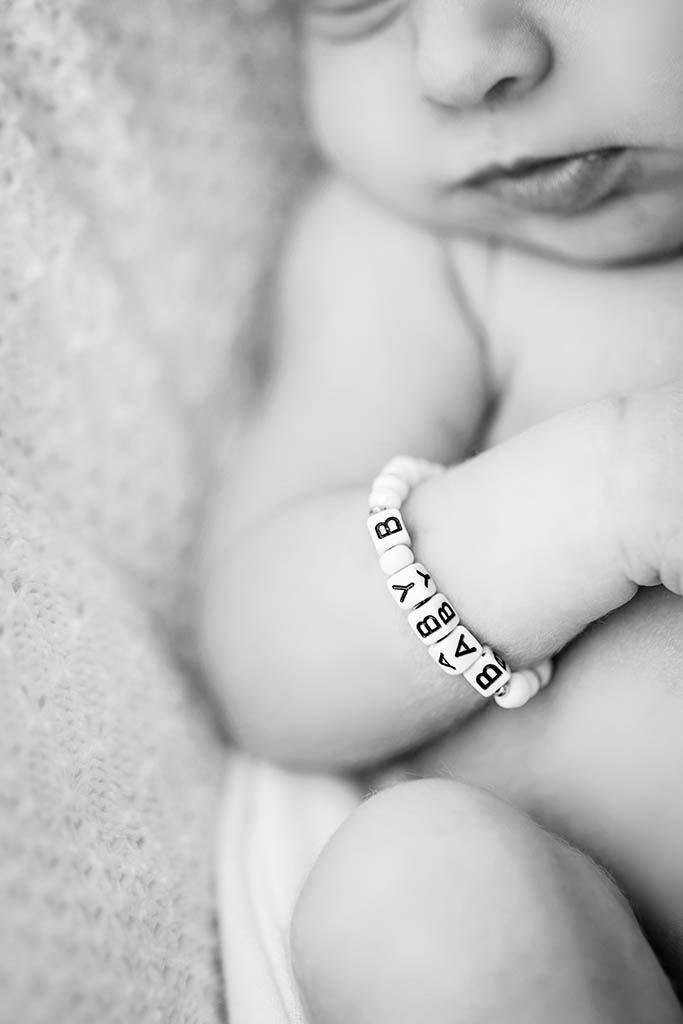 Black and white newborn photo with baby wearing a letter bead bracelet spelling BABY, soft focus portrait.