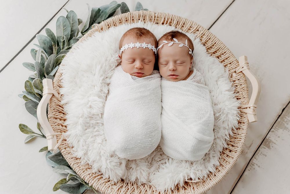 Newborn twin babies swaddled in white wraps with floral headbands by Murrieta newborn twins photographer.