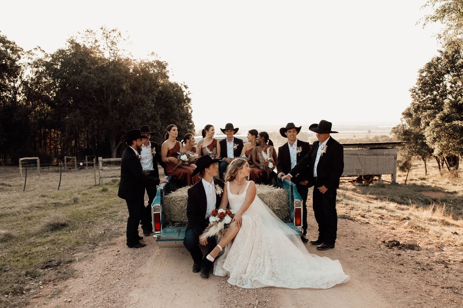 Wedding party in cowboy hats poses around a vintage truck on a rustic ranch at golden hour.