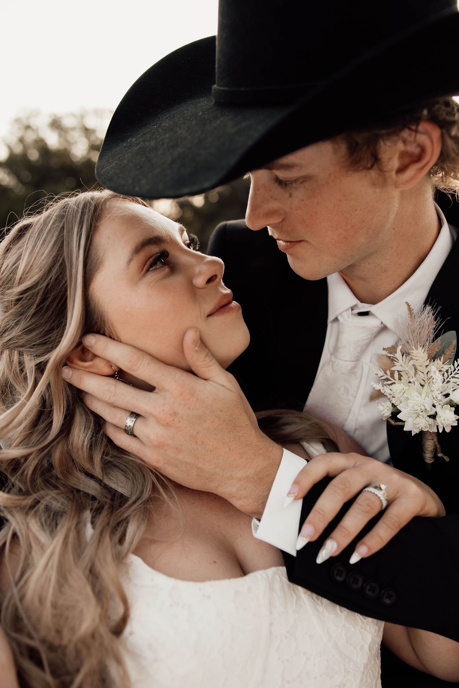 A bride and groom in wedding attire share a romantic moment, the groom wearing a black cowboy hat and boutonniere.
