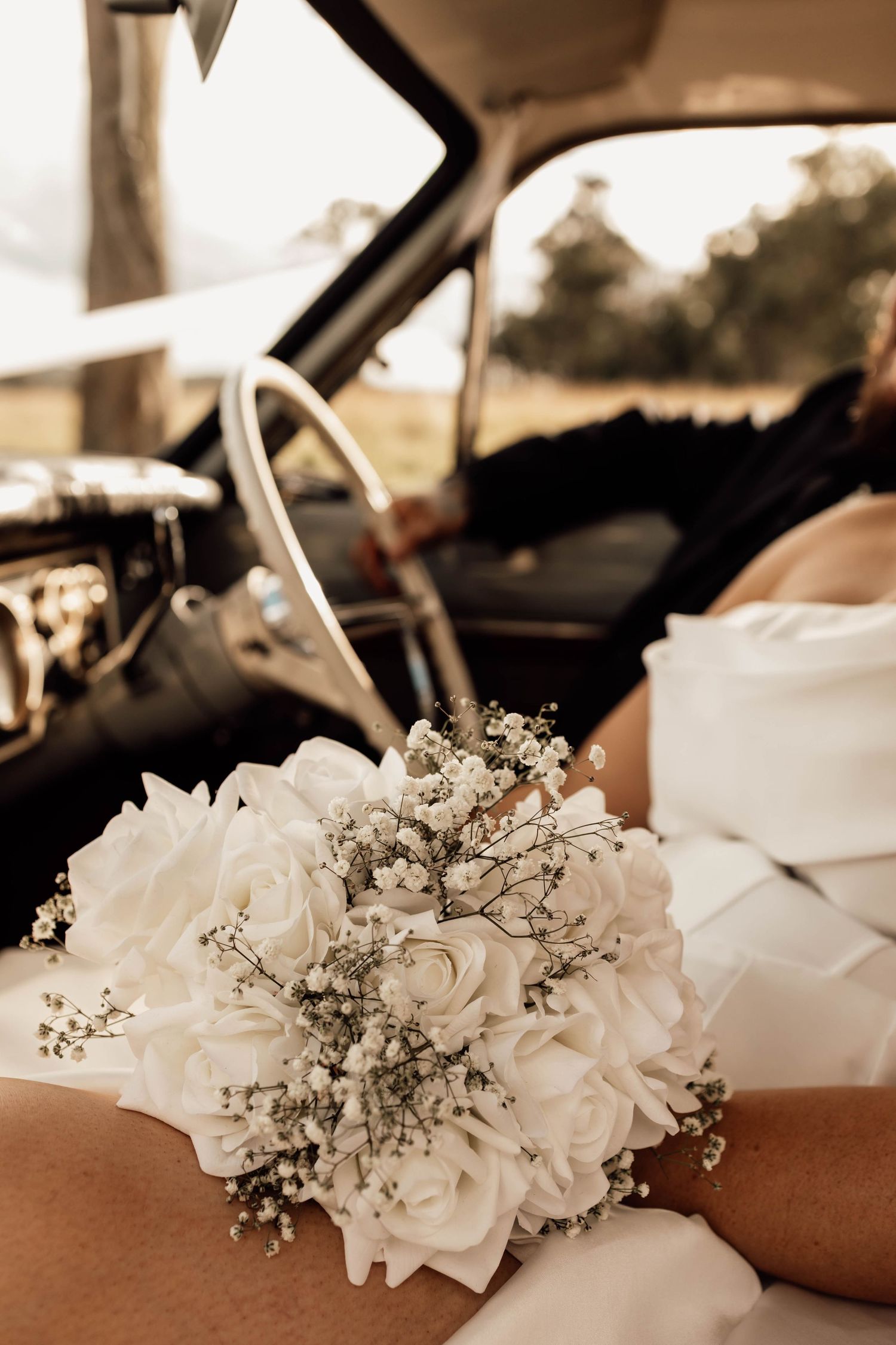 Bride holding white rose and baby's breath wedding bouquet inside a vintage car on her wedding day.